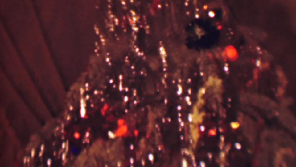 1963 Terre Haute home-movie frame with the camera close to shiny tinsel, small colored bulbs, and dark ornaments on a Christmas tree.