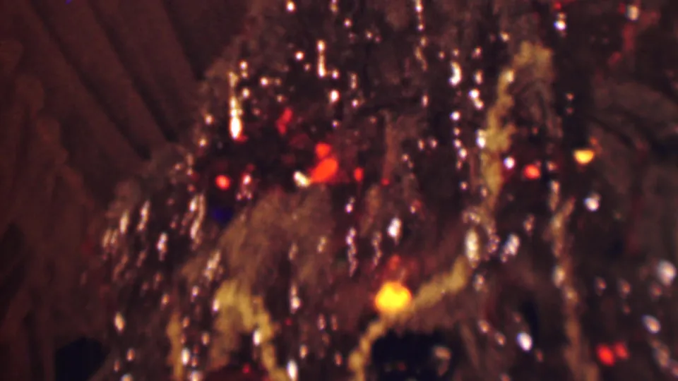 1963 Terre Haute home-movie frame showing the decorated tree from another close angle, with tinsel strands, colored lights, garland, and background curtains.