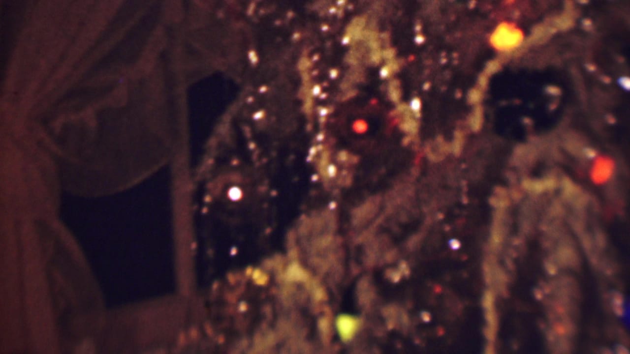 1963 Terre Haute 8mm frame showing a close, soft-focus view of a glossy brown textured object with small red, yellow, and white lights against a dark curtained interior.