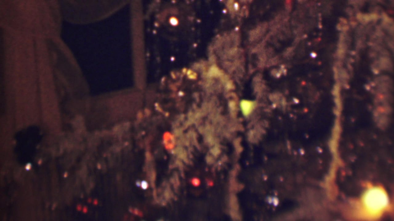 1963 Terre Haute 8mm frame showing reflective brown and tinsel-like strands with small red, yellow, and white lights, with a dark window and curtains in the background.