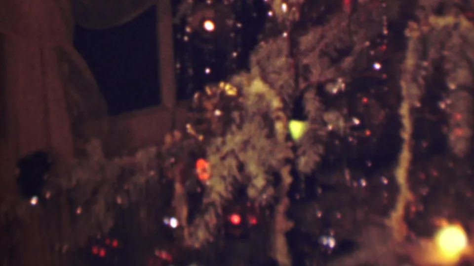 1963 Terre Haute 8mm frame showing reflective brown and tinsel-like strands with small red, yellow, and white lights, with a dark window and curtains in the background.