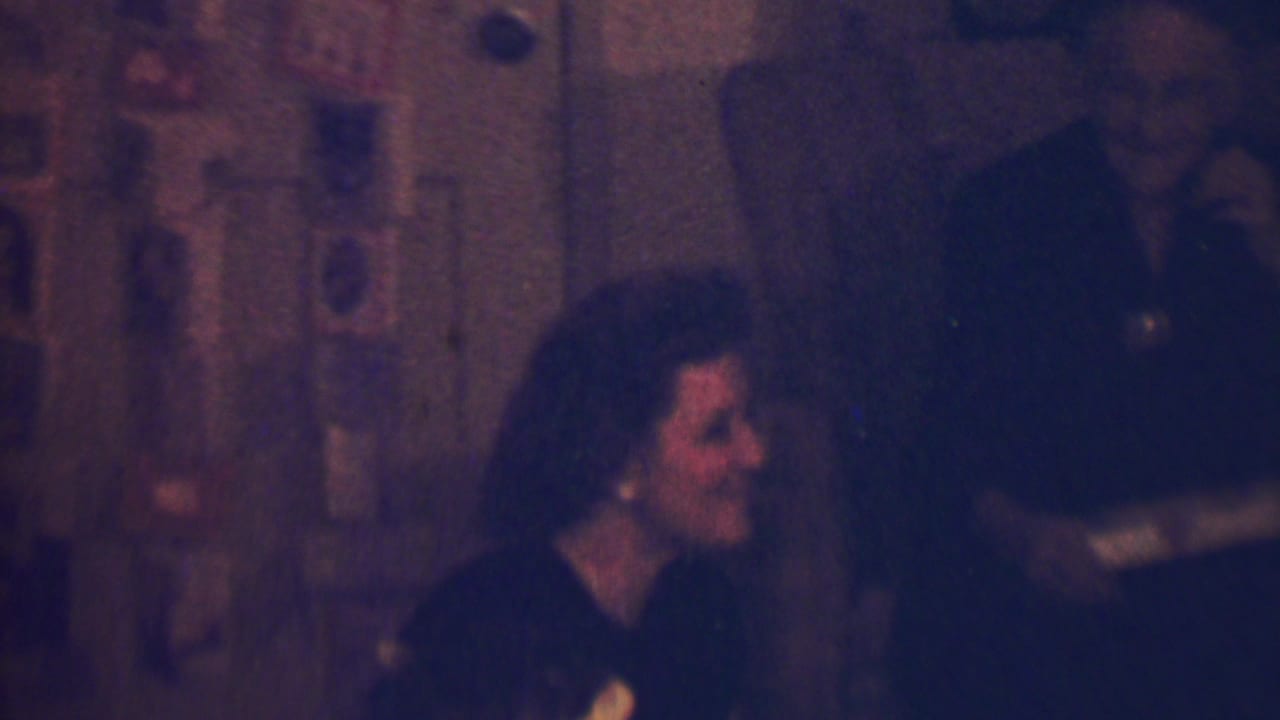 Woman in profile smiles toward someone nearby as a dark doorway or background area fills the right side.