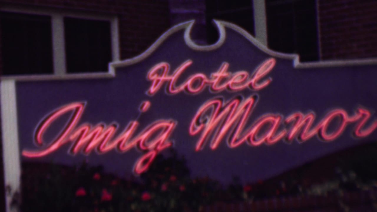 1961 San Diego 8mm frame showing the Hotel Imig Manor sign in red neon script on a purple arched board against a brick facade.