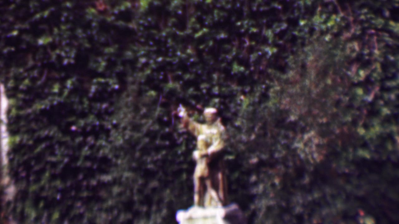 Statue of a man and boy partly framed by foliage and ivy.
