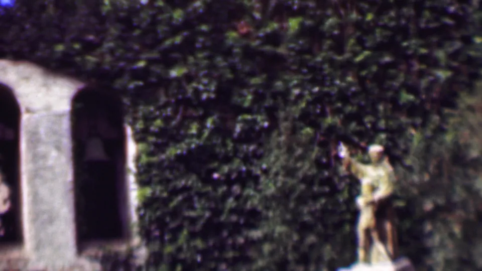 Final 1961 San Diego frame with the stone statue near the right side of the composition, set against ivy, foliage, and a partially visible arched wall.