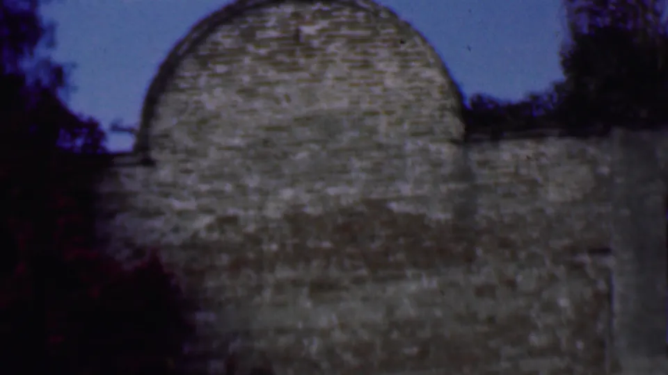 1961 San Diego home-movie frame showing a rounded masonry gable or wall section below sky, with dark trees framing the stone surface.