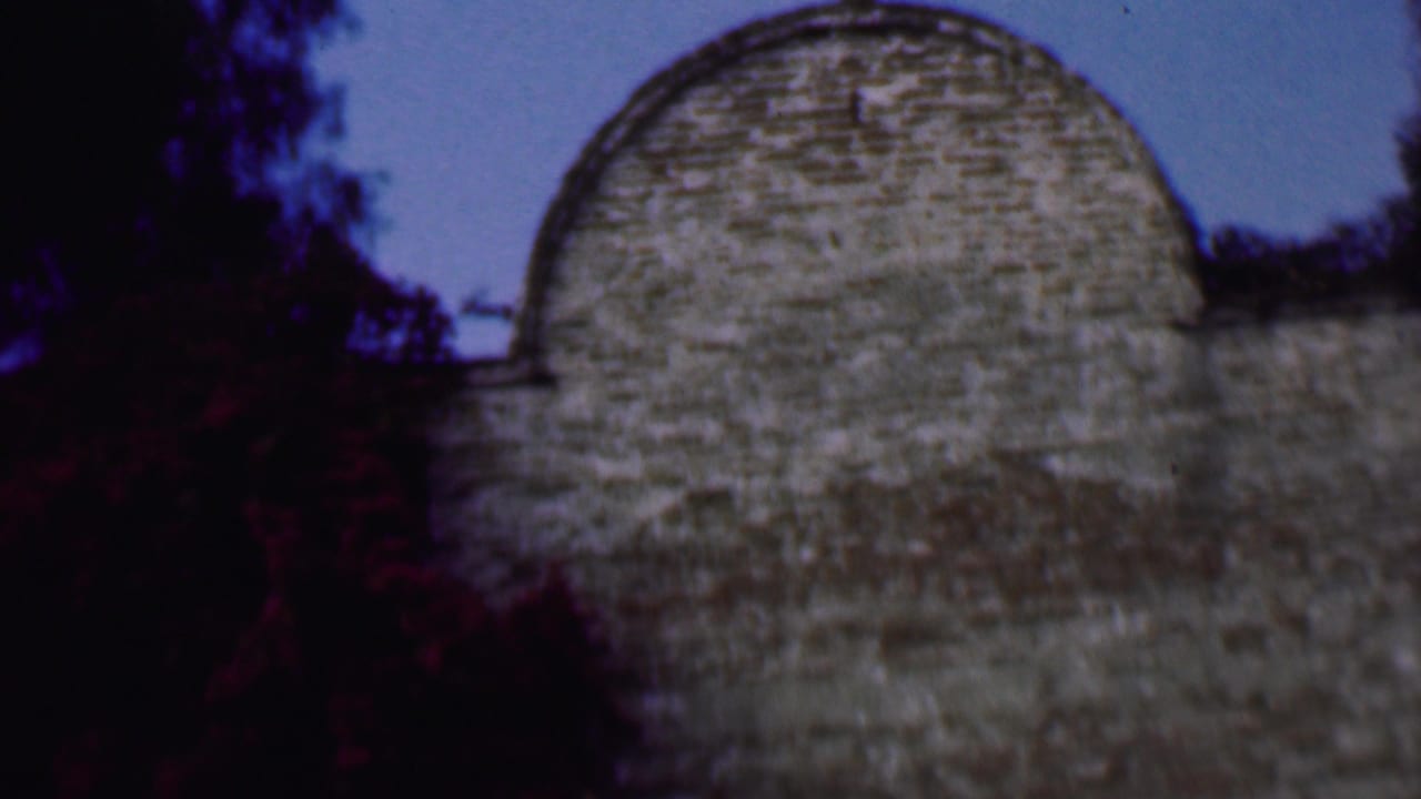 1961 San Diego 8mm frame showing a pale stone church dome partly obscured by dark tree silhouettes against a blue sky.