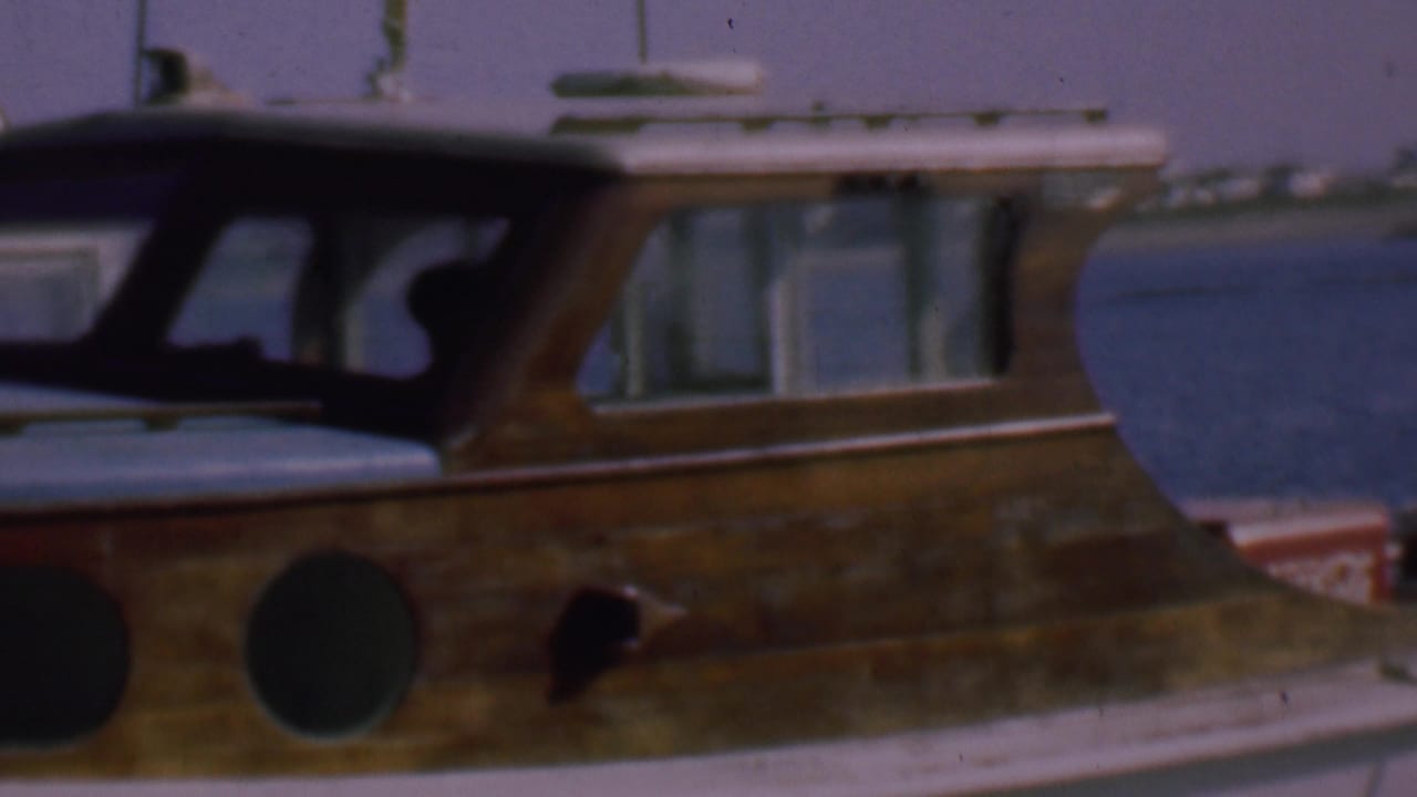 1961 San Diego marina view of a weathered wooden motorboat with round portholes, dark cabin windows, and background boat structures.