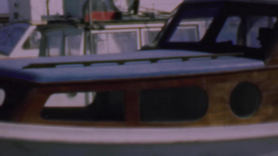 1961 San Diego marina shot of the motorboat side, showing a long dark cabin window, rounded porthole, varnished wood trim, and nearby boat windows behind it.