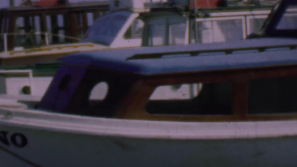 End frame from the 1961 San Diego marina clip showing the boat cabin at an angle, with dark rounded windows, pale hull, and another vessel in the background.