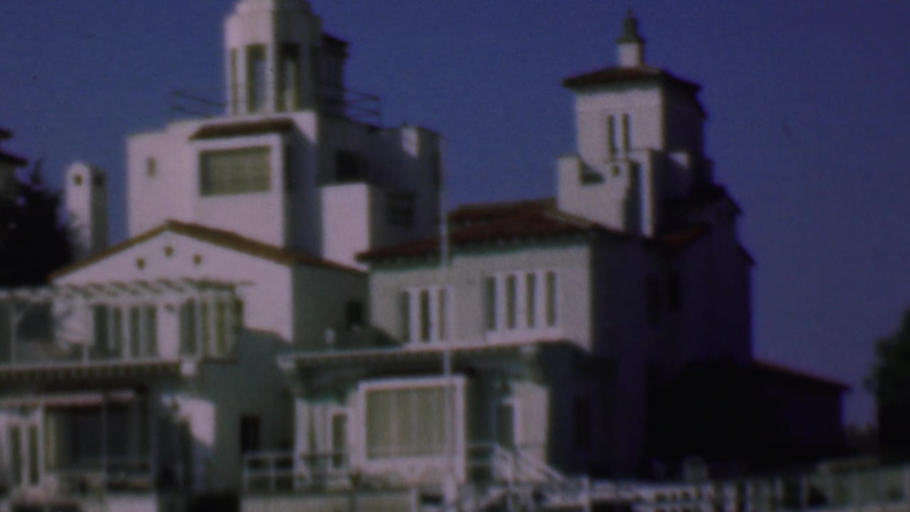 1961 San Diego home-movie frame showing white stucco residential buildings with red tile roofs, balconies, shuttered windows, and tower forms under a deep blue sky.