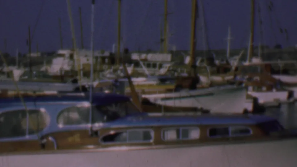 1961 San Diego marina view with sailboat masts, small motorboats, cabin boats, dock structures, and a hazy shoreline beyond the harbor.