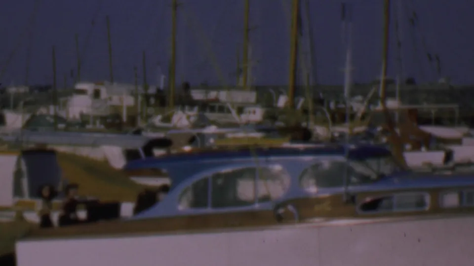 1961 San Diego harbor frame showing moored boats, tall masts, dockside structures, and small incidental people near the lower center of the frame.