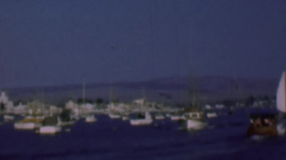 1961 8mm San Diego harbor view with sailboats and small vessels anchored in calm water beneath a deep blue sky.