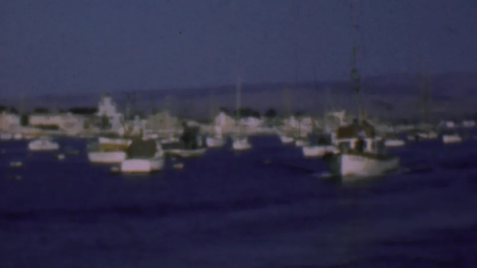 1961 San Diego harbor view with a small fishing boat in the foreground, other boats scattered across calm water, and a hazy shoreline beyond.
