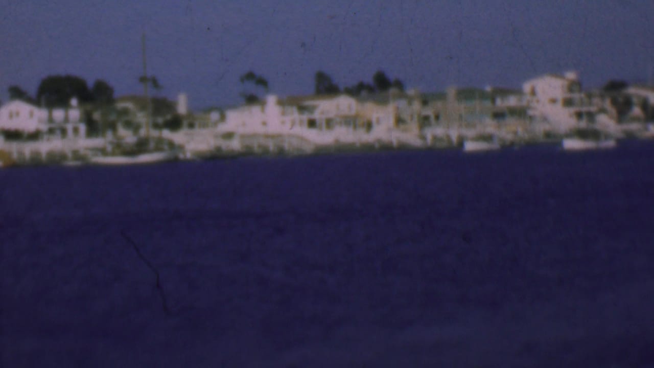 Waterfront buildings and small boats line a harbor under a dusky blue sky.