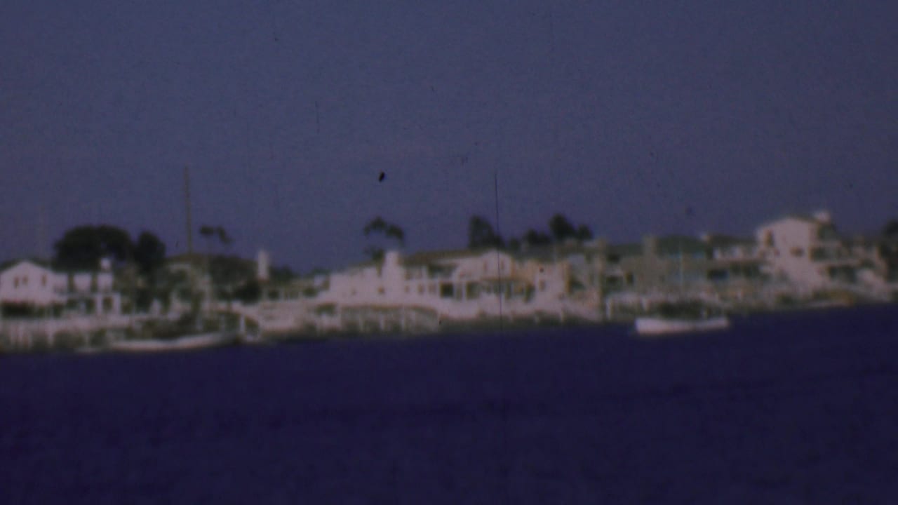 Small boats near pale waterfront houses under a blue sky.