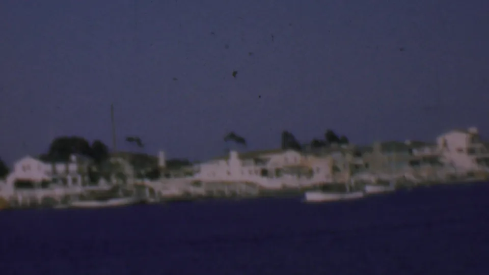 End frame of a 1961 San Diego waterfront view, with a small boat near pale shoreline houses and docks across calm water.