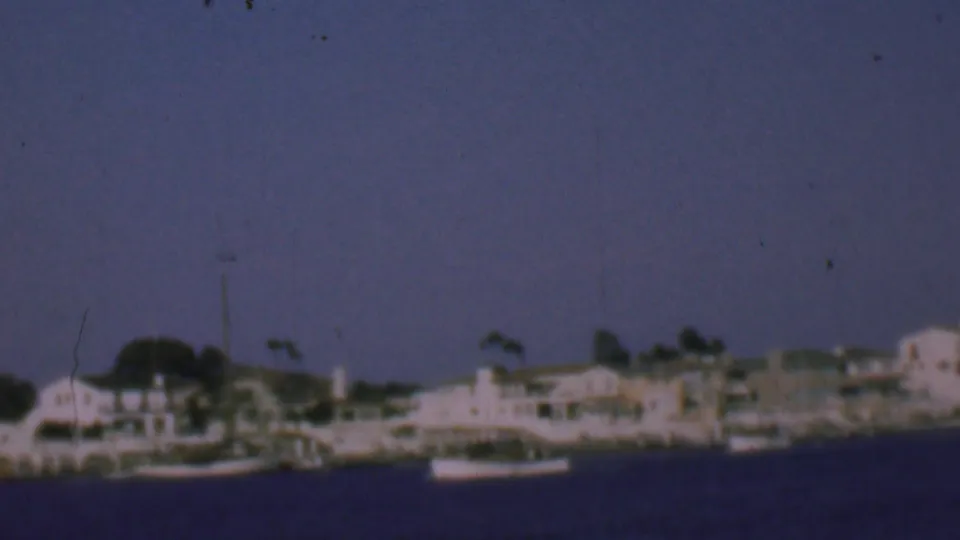 Aged 8mm view of San Diego waterfront homes and moored boats, with blue-purple color cast and handheld motion blur from the moving boat.
