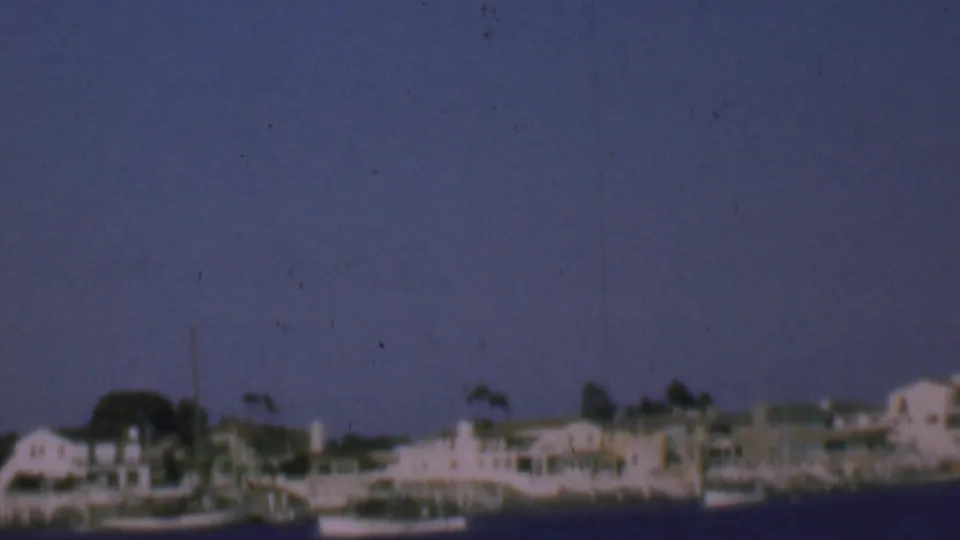 Final 1961 San Diego coastal frame showing distant waterfront residences, small boats near the shore, open blue sky, and visible home-movie film wear.