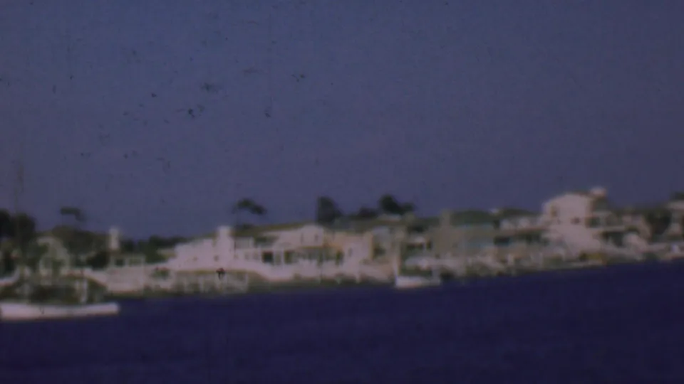 Distant San Diego waterfront homes and a small boat appear along the shore in soft, grainy 8mm color.