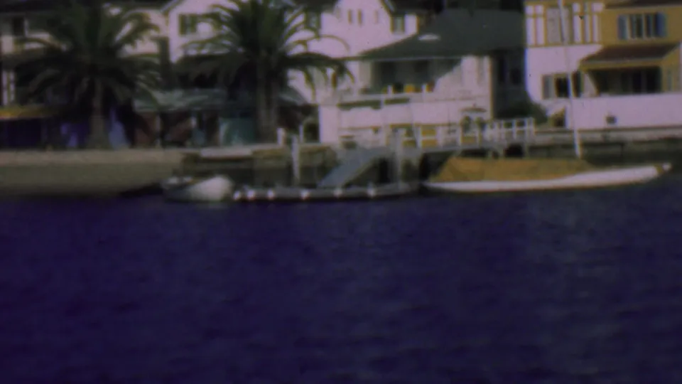 1961 San Diego waterfront residences appear closer in frame, with palms, private piers, a seawall, and small boats along the waterline.