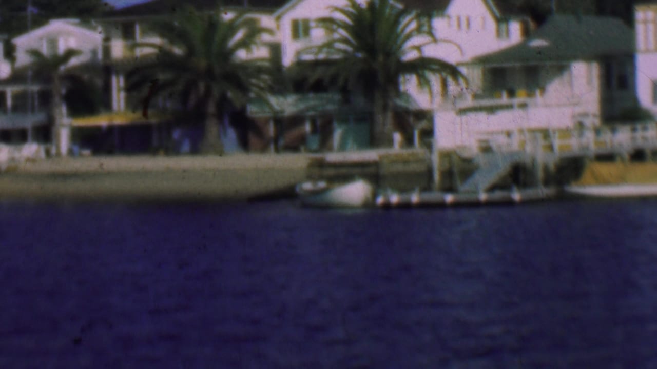 1961 San Diego waterfront view showing white residential houses, palm trees, docks, and a small boat seen from across the water.