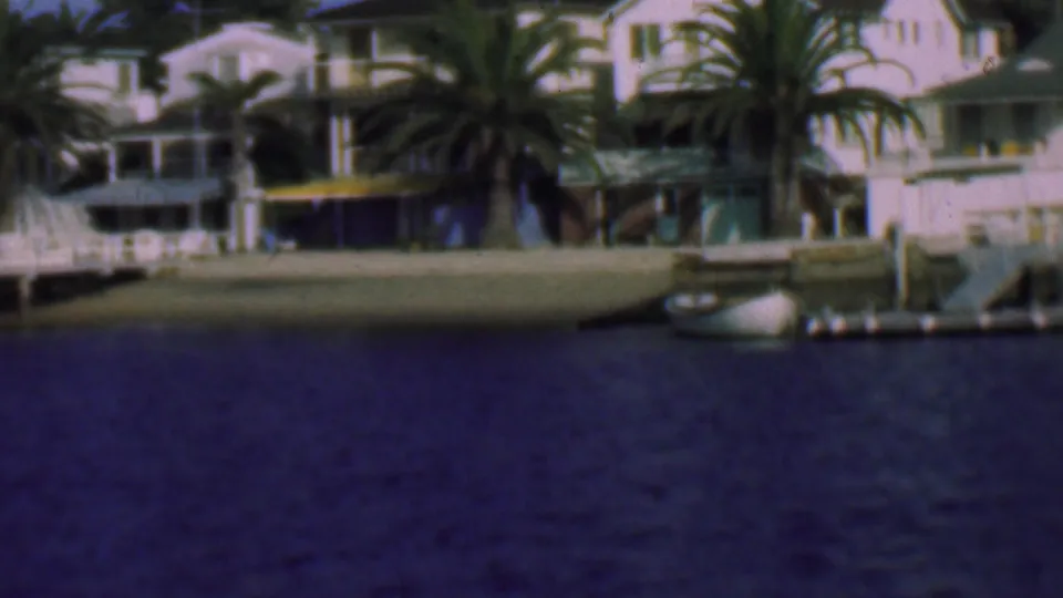 1961 San Diego shoreline with white homes, large palms, small piers, and a moored boat along the residential waterfront.