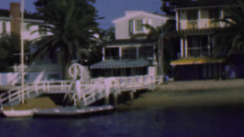 1961 San Diego residential shoreline showing a white dock in front of palm trees, houses, awnings, and calm water.