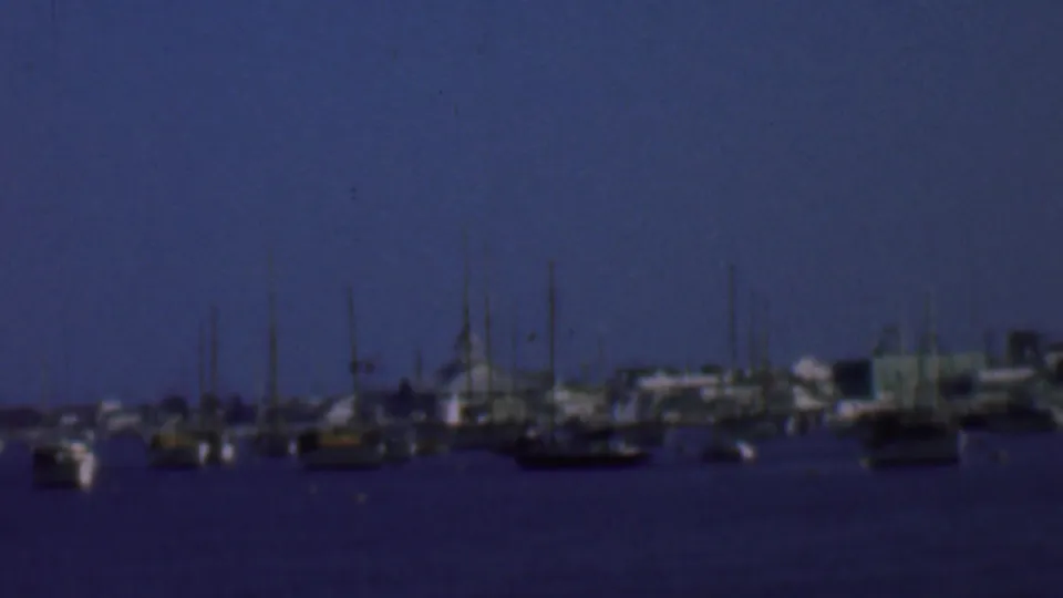 1961 San Diego-area 8mm frame showing a marina at dusk with sailboats and yachts at anchor, their masts silhouetted against a blue sky.