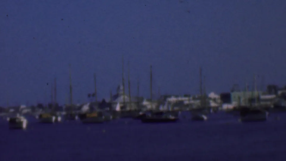 1961 San Diego-area 8mm frame of a quiet marina with anchored boats, clustered masts, waterfront structures, and deep blue twilight color.
