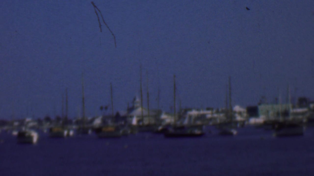 1961 San Diego harbor view with small boats, clustered masts, low waterfront structures, and soft blue 8mm color.