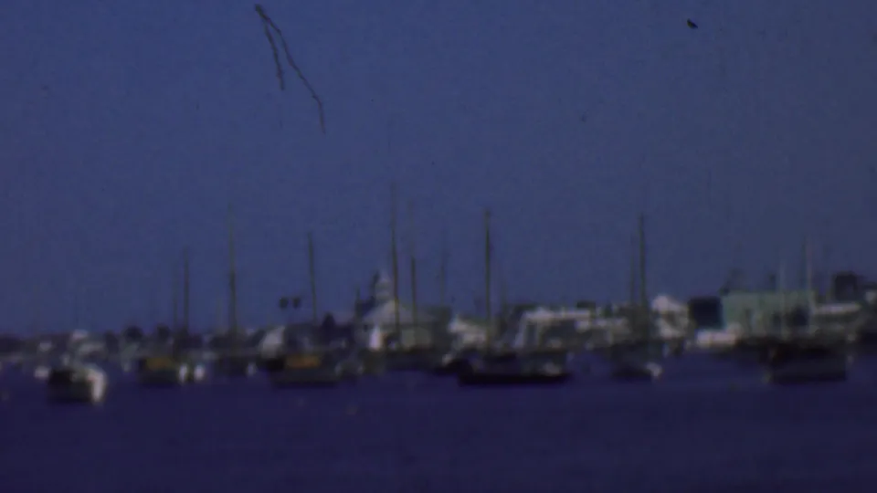 1961 San Diego harbor view with small boats, clustered masts, low waterfront structures, and soft blue 8mm color.