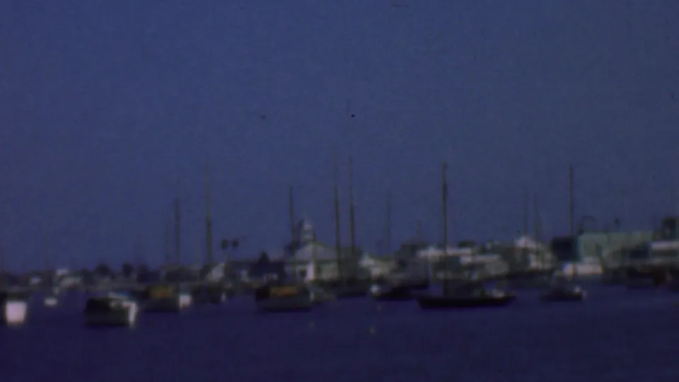1961 San Diego harbor frame showing moored sailboats and yachts, vertical masts, calm water, and distant waterfront forms in soft 8mm texture.