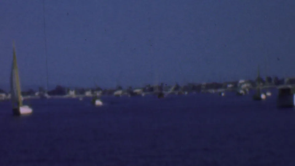 1961 San Diego bay view with a central sailboat, scattered anchored boats, soft shoreline detail, and blue 8mm color shift.