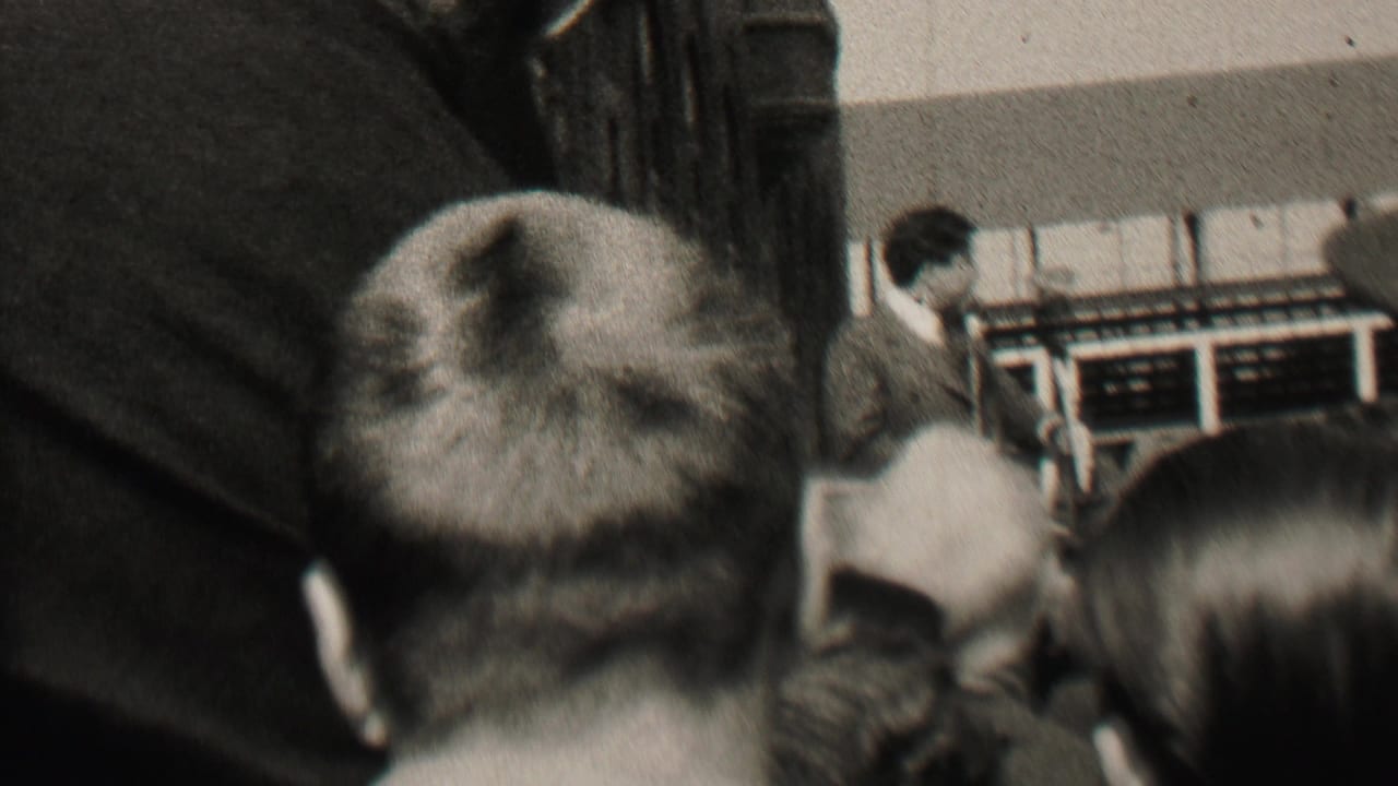 1937 Albany 8mm frame showing a crowded indoor meeting from behind the audience, with a suited man near a podium at the front of the room.