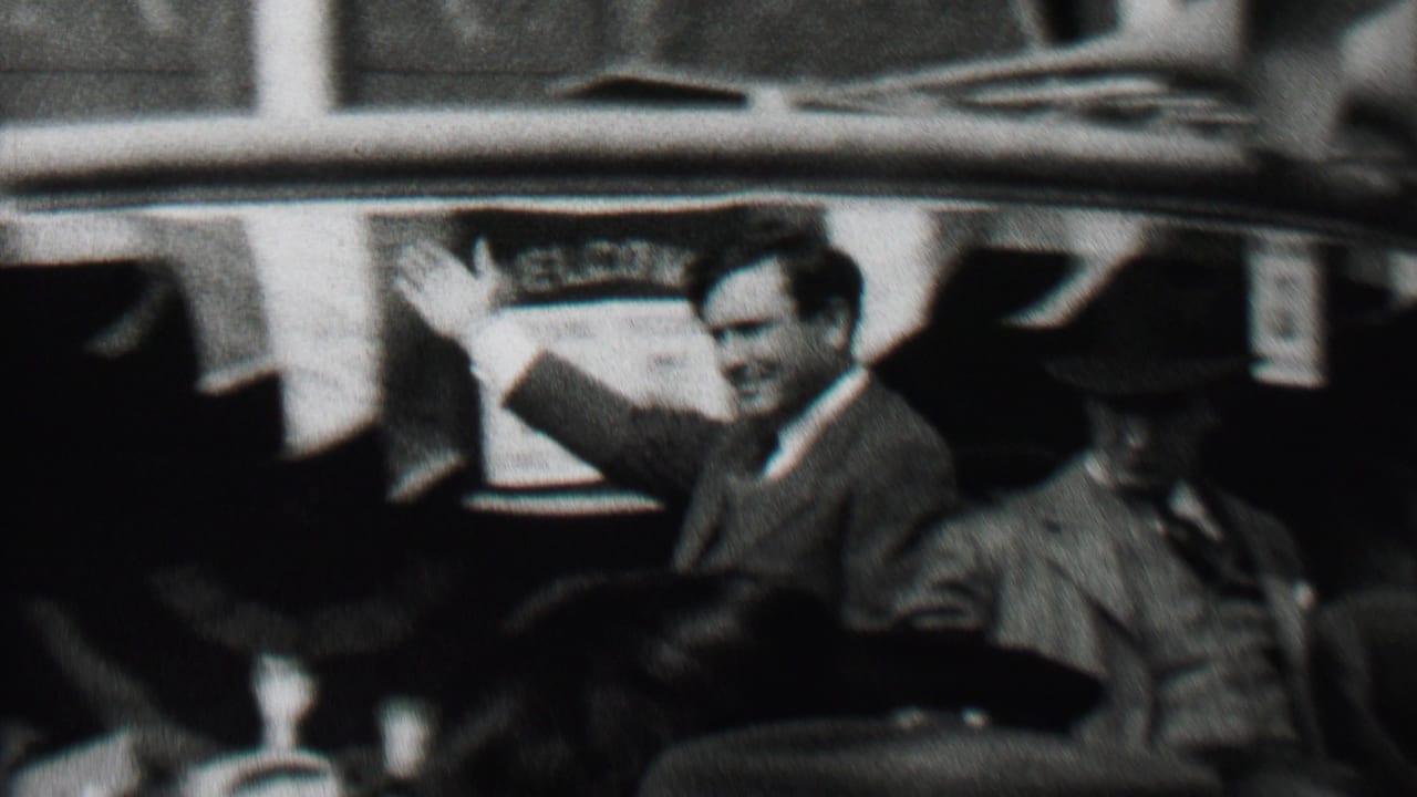 In Albany, New York, in 1937, a suited campaign figure appears to wave from an open car while men in hats sit nearby and spectators crowd the street.