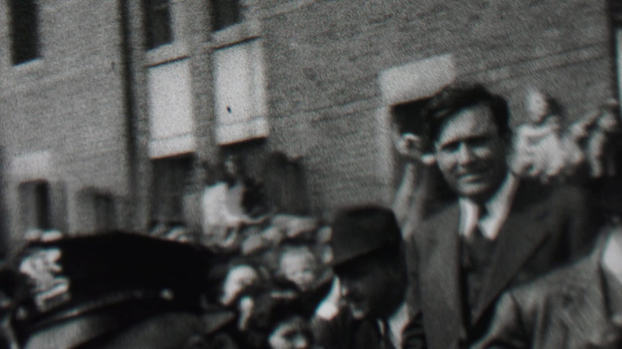 In Albany, New York in 1937, a suited man waves from within a dense public crowd as police officers and onlookers stand near a brick building entrance.
