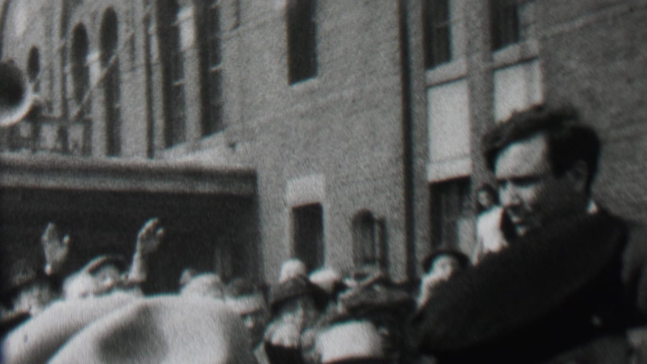 Crowd gathers near police and a brick building as the waving man remains in view.