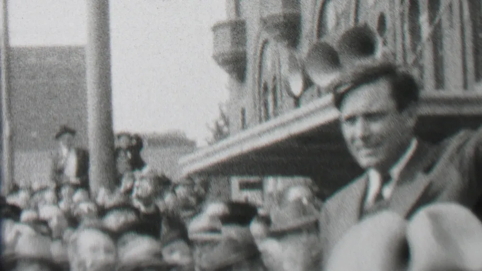The final frame shows the suited man closer to the camera at the edge of the Albany crowd, with police, onlookers, and a canopy attached to a brick building visible behind him.