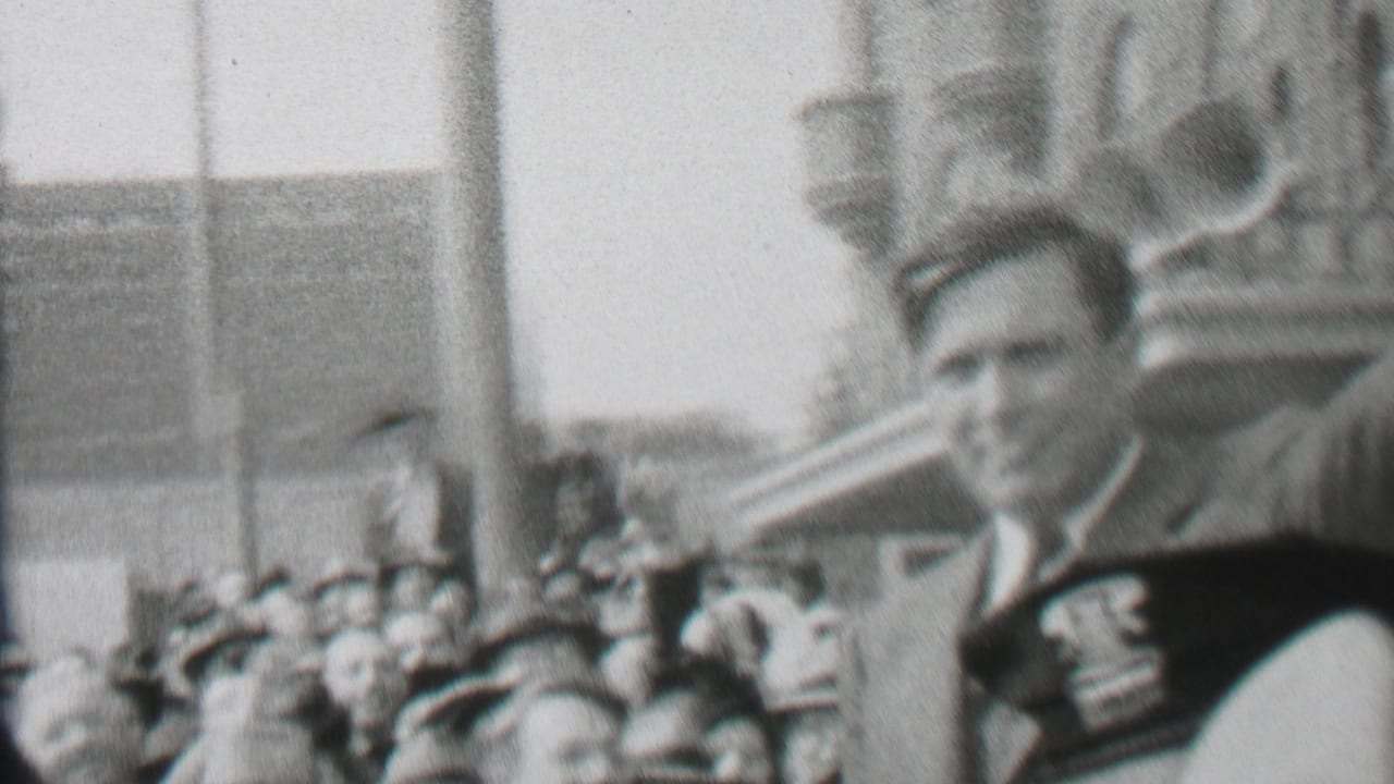 In Albany, New York home-movie footage from 1937, bundled adults stand and move near a snowy park bridge while one man appears close to the camera.