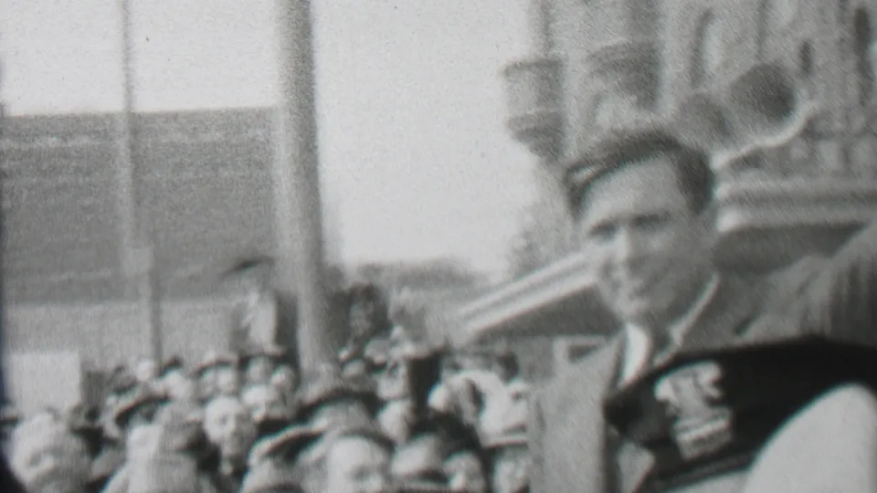 In Albany, New York home-movie footage from 1937, bundled adults stand and move near a snowy park bridge while one man appears close to the camera.
