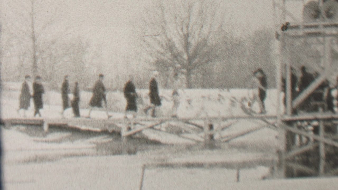 A line of pedestrians walks across a snowy bridge beside a structural framework.