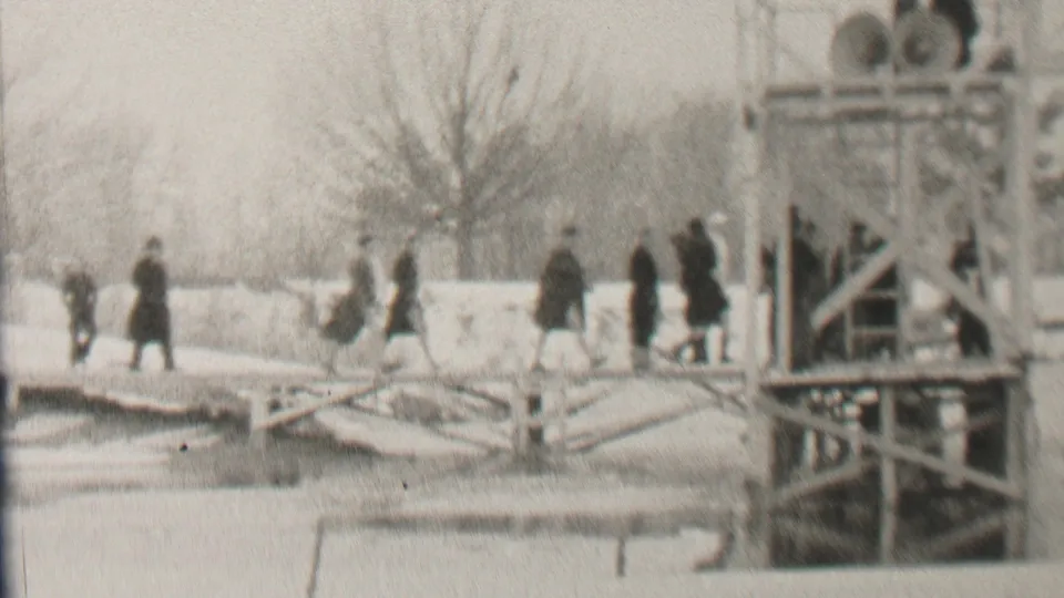 In 1937 Albany, New York, pedestrians in coats and hats cross the snow-covered bridge near a right-side framework, while bare winter trees and a frozen-looking waterway remain visible.
