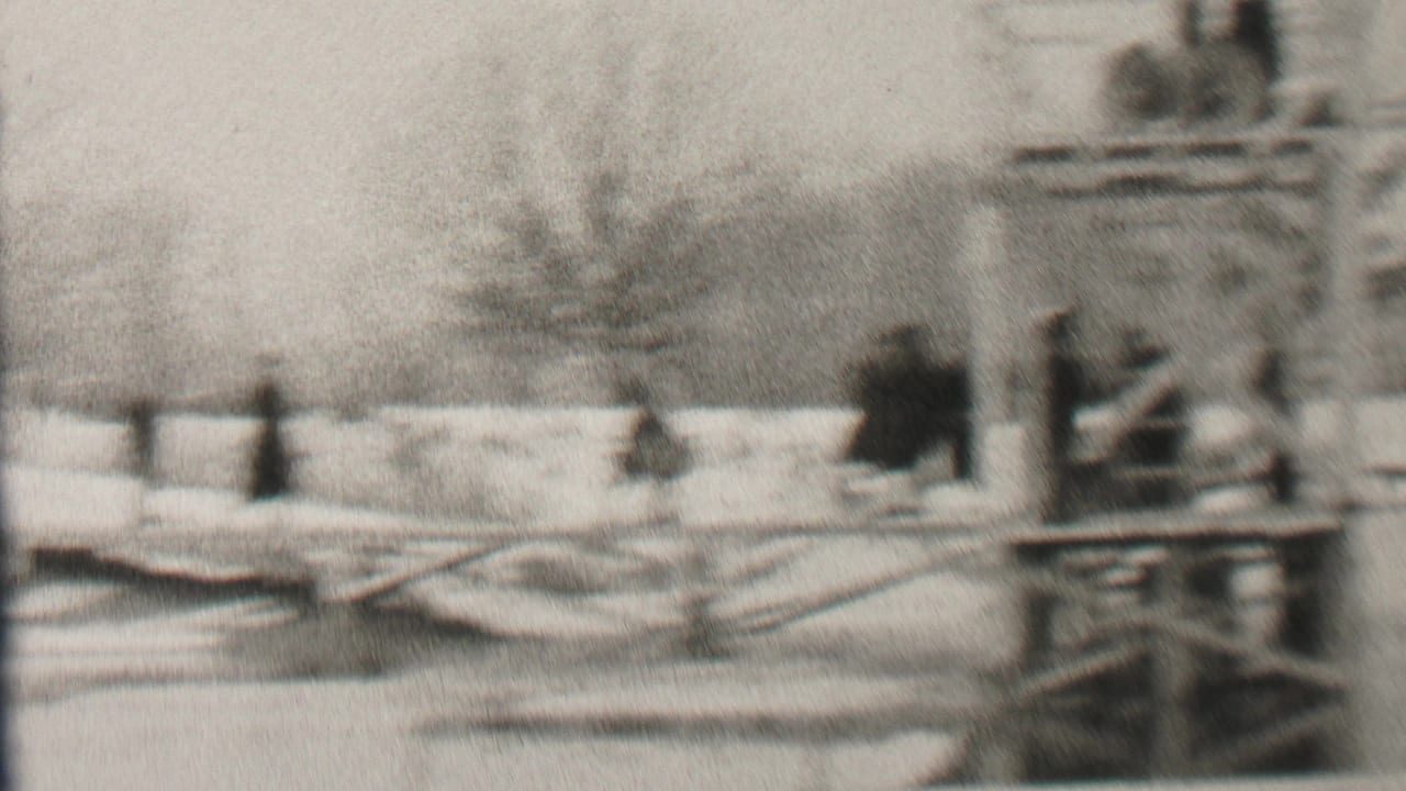 Soft black-and-white 1937 Albany home-movie frame showing a snowy waterfront area with bundled figures near wooden railings and a small platform.