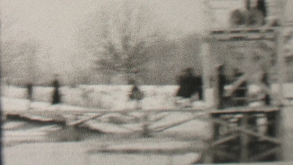 Soft black-and-white 1937 Albany home-movie frame showing a snowy waterfront area with bundled figures near wooden railings and a small platform.