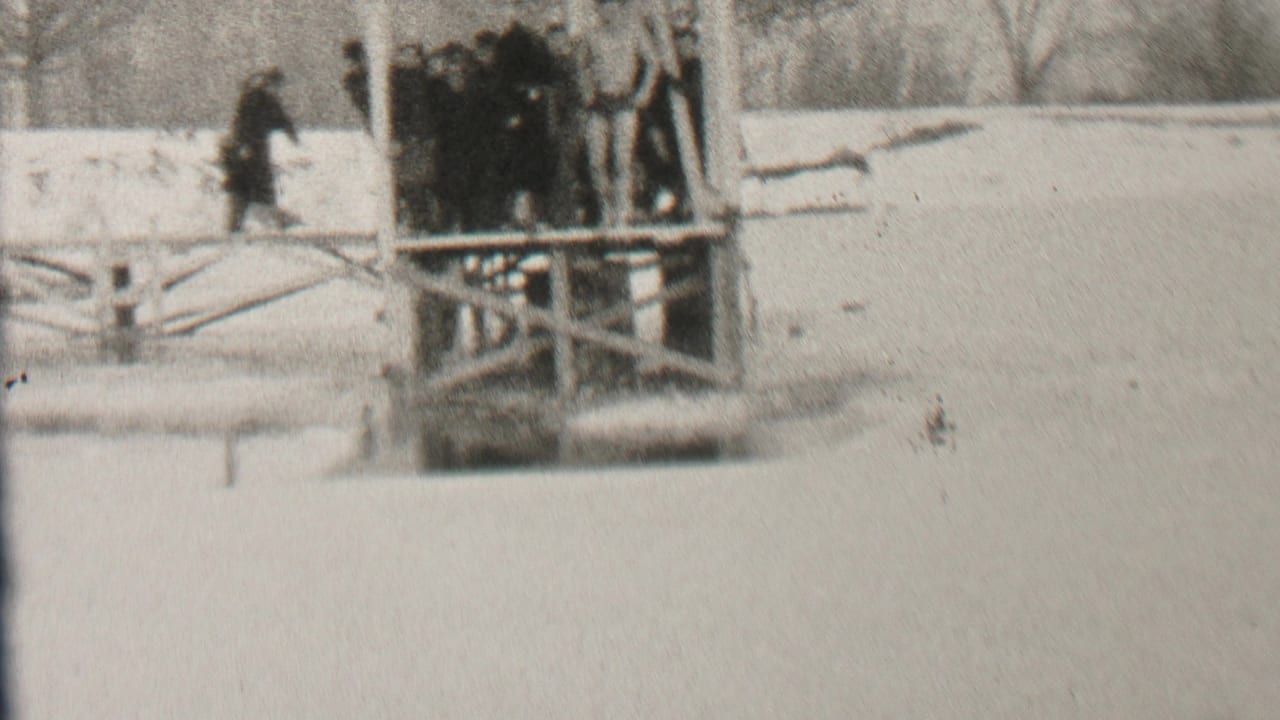 Black-and-white frame from Albany in 1937 showing bundled people gathered on a wooden platform beside a snow-covered winter shoreline.