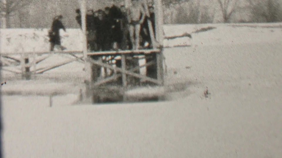 Black-and-white frame from Albany in 1937 showing bundled people gathered on a wooden platform beside a snow-covered winter shoreline.