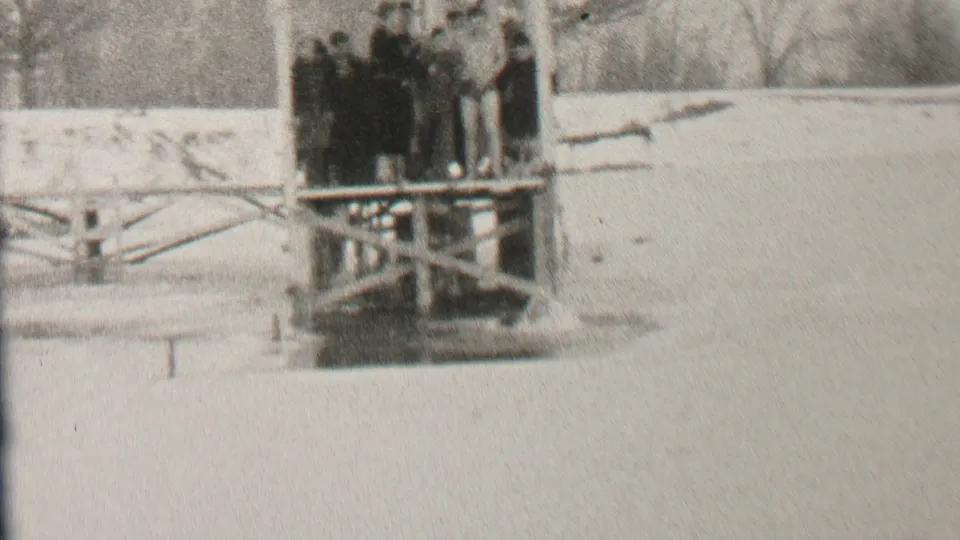 1937 Albany home-movie still showing a clustered group in winter clothing on a wooden platform beside snow and pale water or ice.