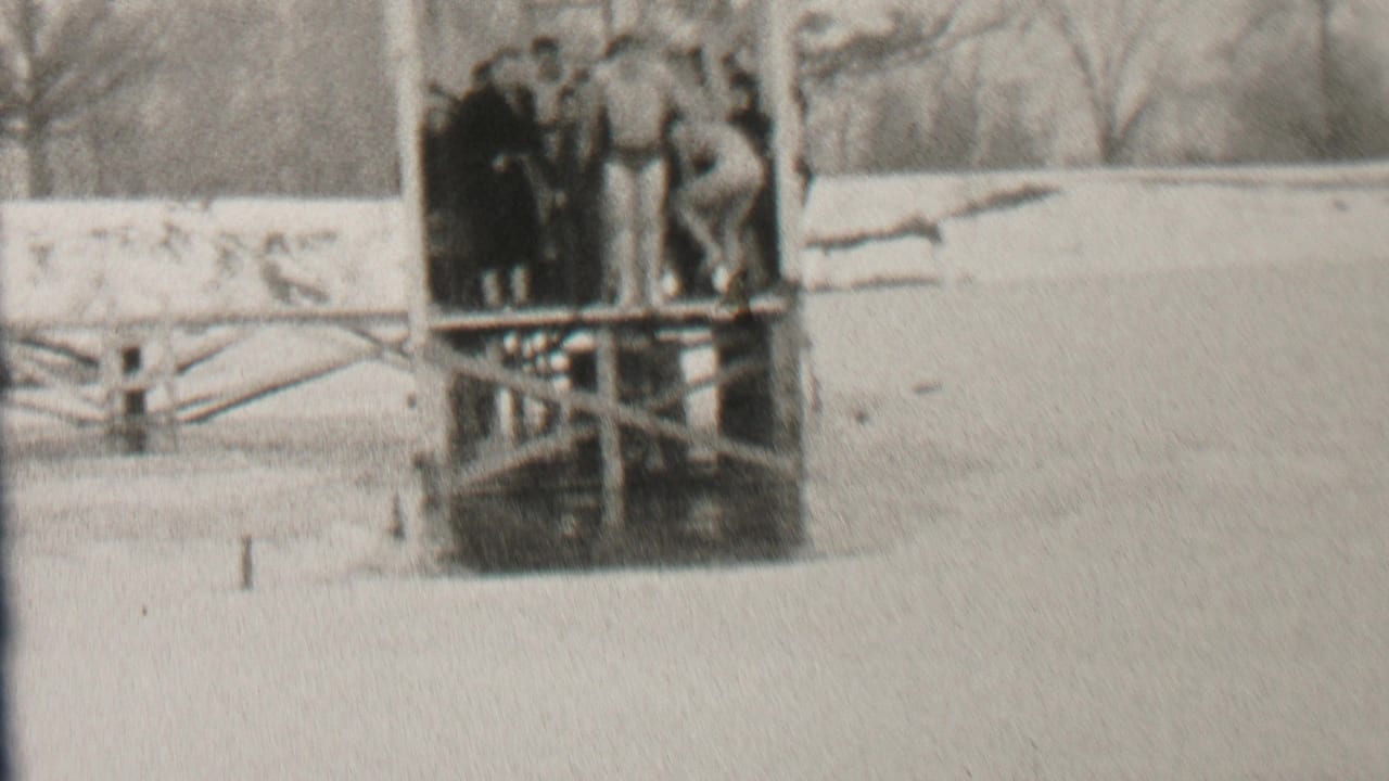 A person dives headfirst from a wooden platform as others watch in the snow.